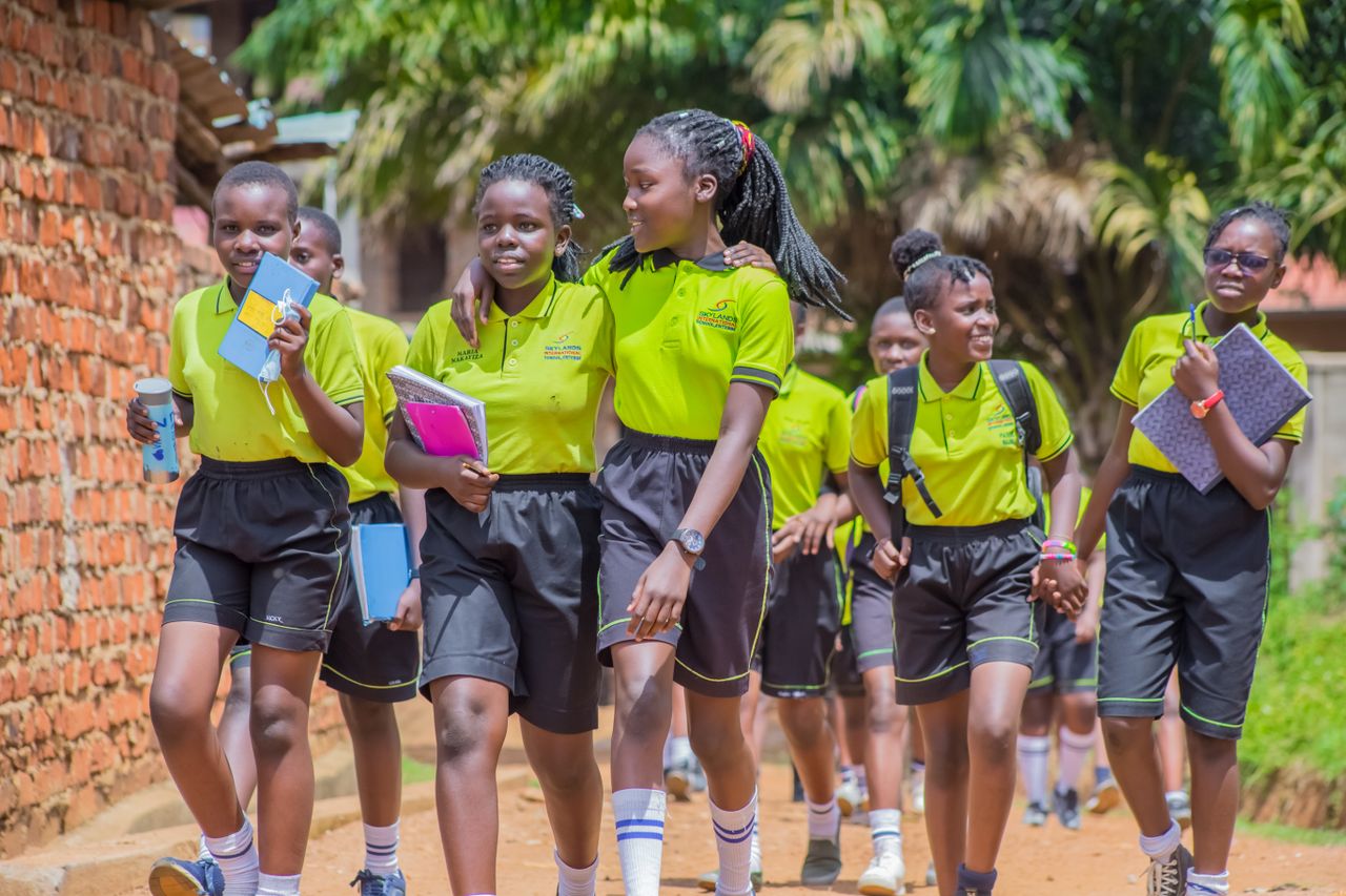Group of smiling Ugandan students walking outdoors in school uniforms.