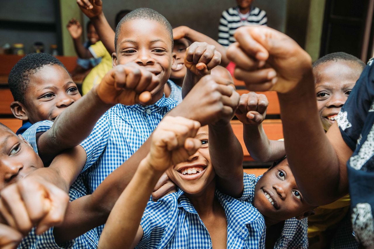 Group of smiling African children showing unity with raised fists in a classroom setting.