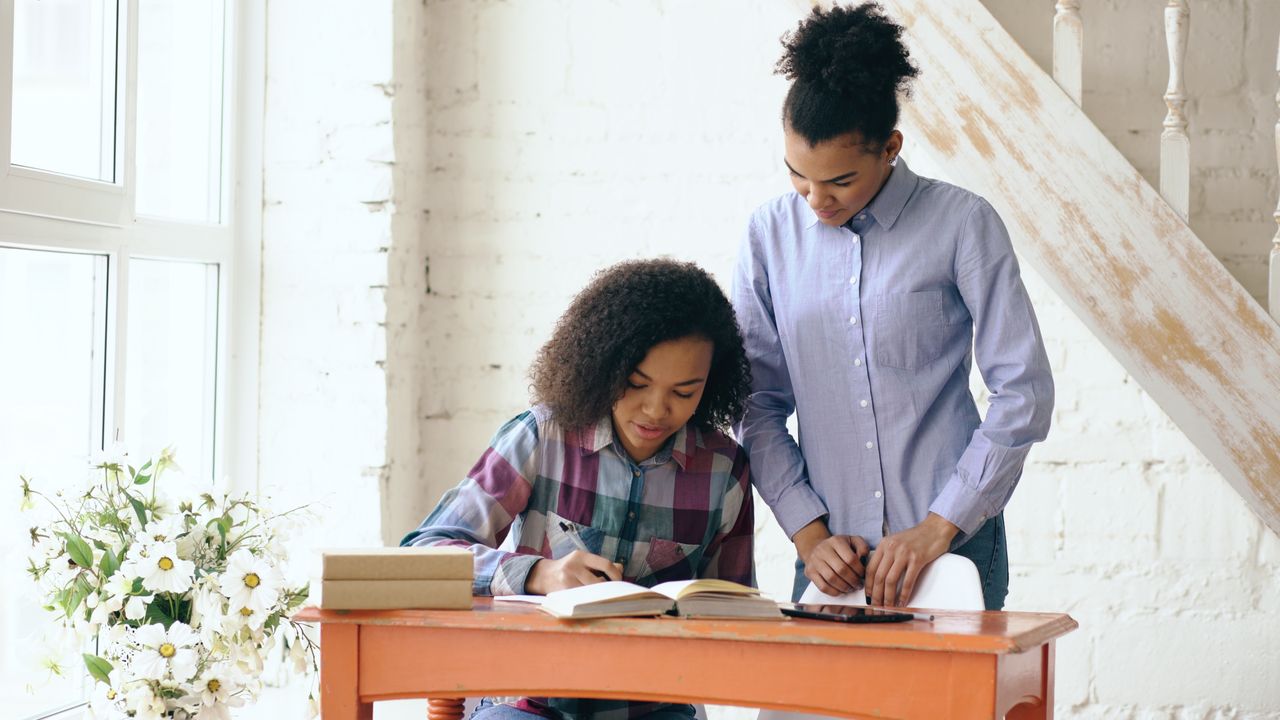 Mother helping daughter with homework at home in warm daylight.