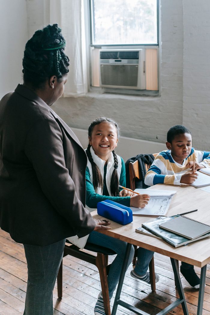 African American female teacher standing near school bench and talking to smiling multiracial classmates